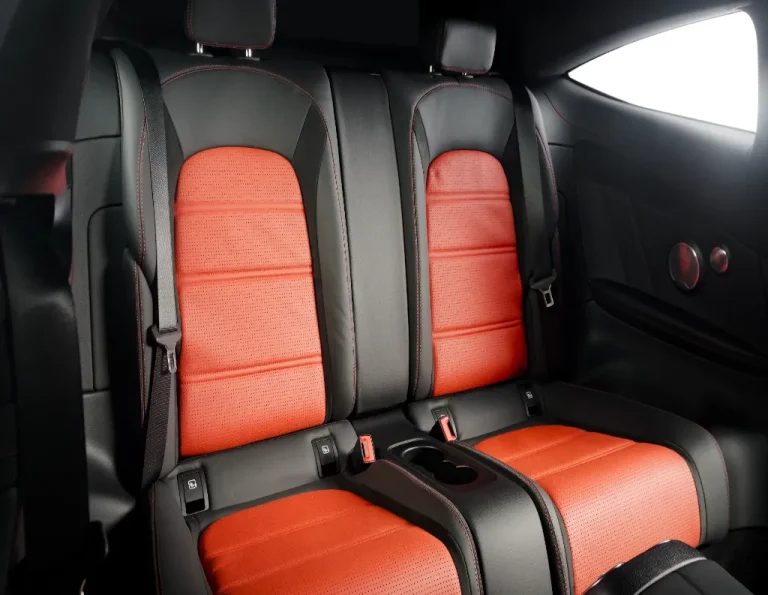 Rear seats of a car featuring black and red leather upholstery, with two headrests, seat belts, and a central armrest equipped with cup holders. The interior is modern and stylish.