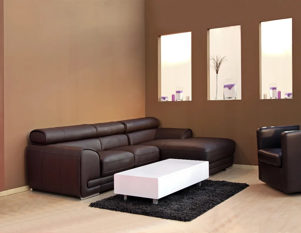 Modern living room with a dark brown sectional sofa, matching armchair, white rectangular coffee table on a black rug, and three backlit wall niches displaying minimalist decor.
