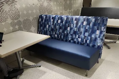 A blue cushioned booth with a patterned blue backrest sits next to a white table in a modern room with light-colored, geometric-patterned walls and flooring.