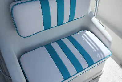 A boat seat with white and teal striped cushions and white armrests, illuminated by natural sunlight.